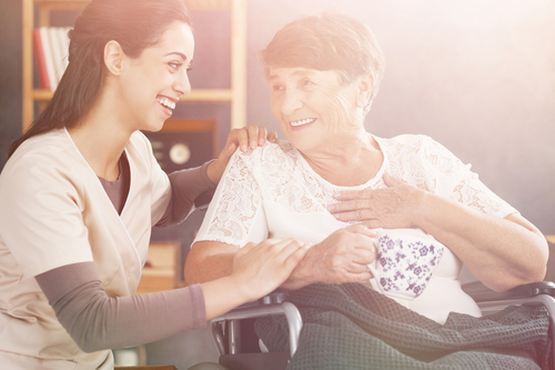 Young nurse knelt down smiling at woman in wheelchair