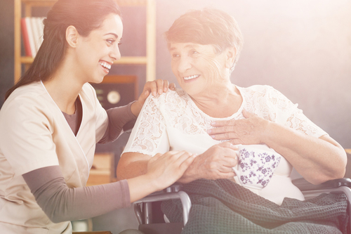 Young nurse knelt down smiling at woman in wheelchair 